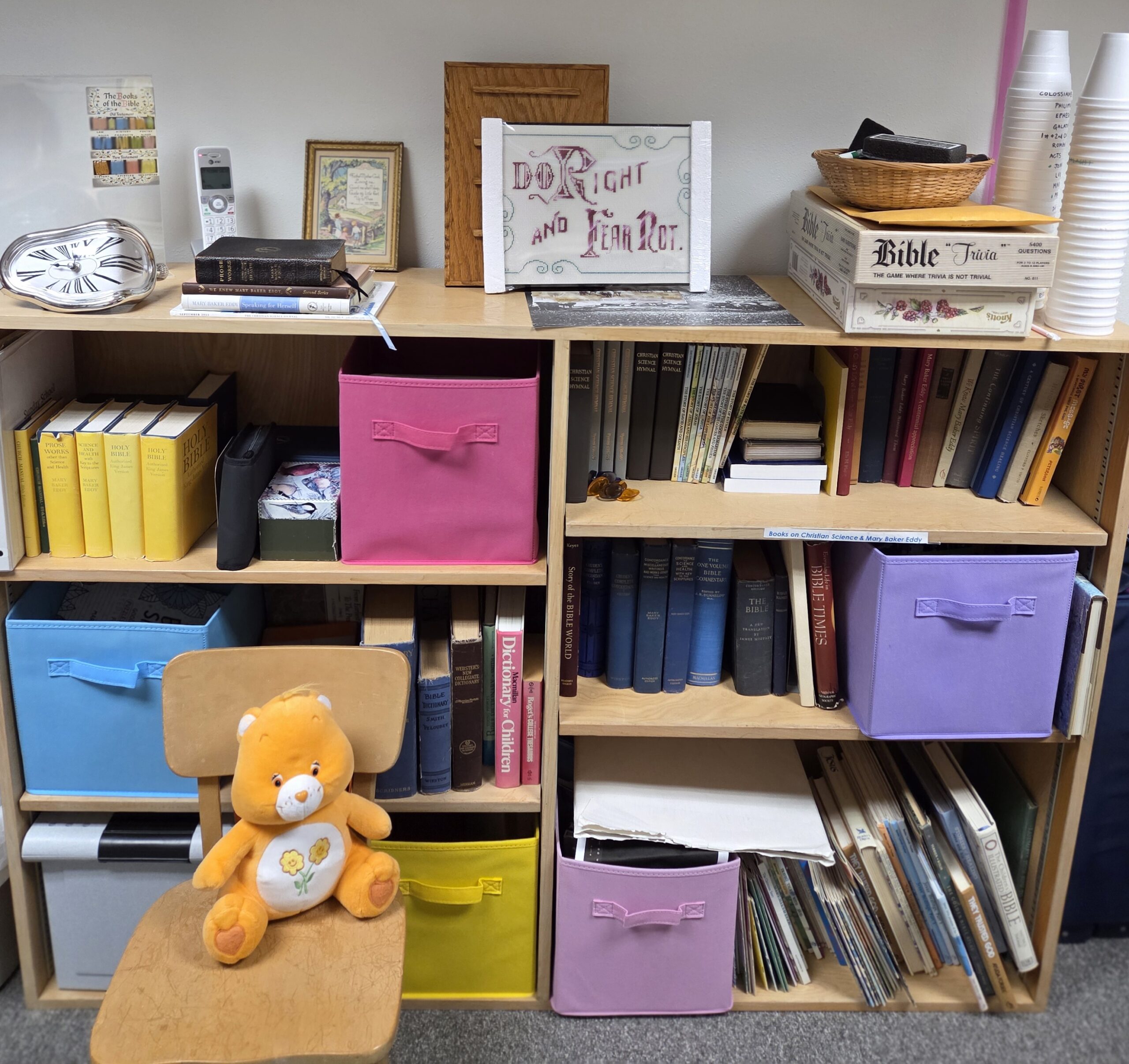 Sunday school resources on a shelf unit with books and colorful bins.